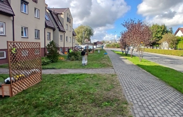 Widok na ulicę Graniczną z nowymi drewnianymi donicami i pergolami, posadzonymi na trawniku przed budynkami mieszkalnymi.