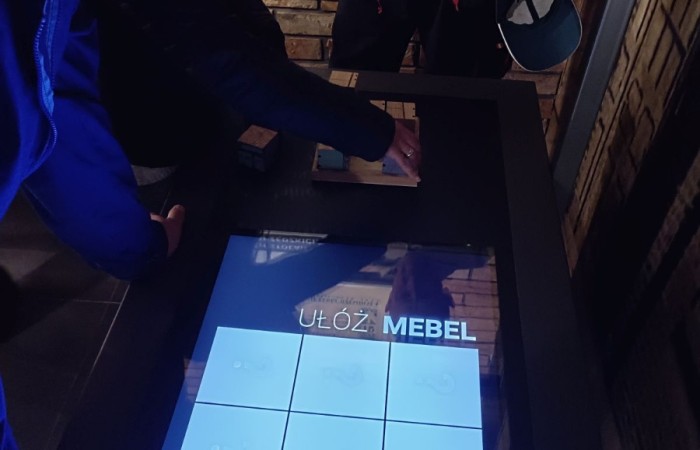 osoba pochyla się nad ekranem multimedialnym