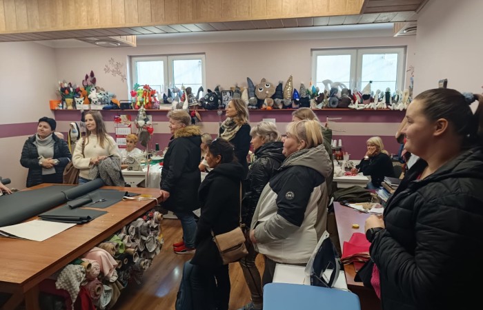 Grupa osób z Centrum Integracji Społecznej podczas wizyty w pracowni rękodzieła, otoczeni przez różnorodne maskotki i dekoracje.