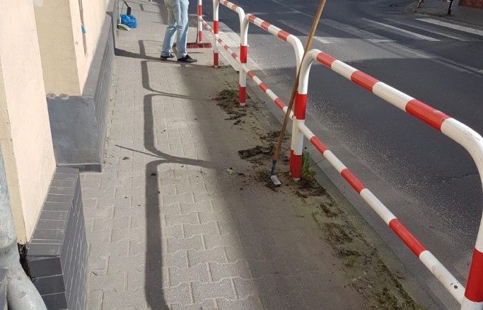 osoba sprząta kostke brukową przed klubem integracji społęcznej